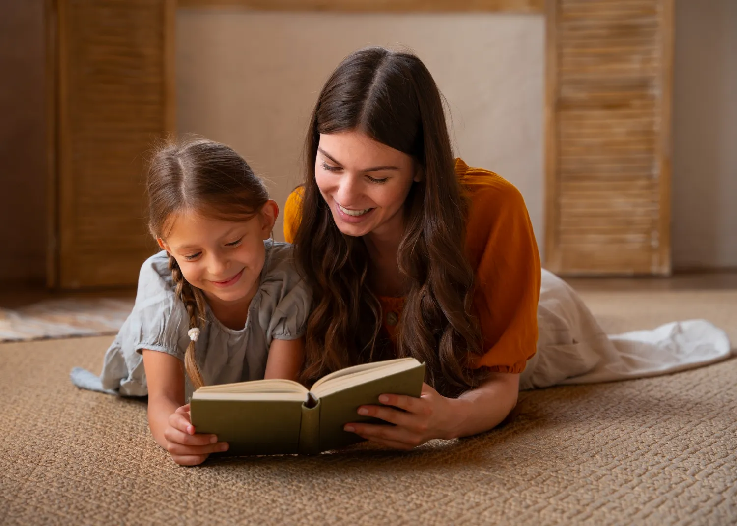 Mujer y niña leyendo un libro en el suelo, disfrutando de un momento de aprendizaje y conexión en un ambiente acogedor.